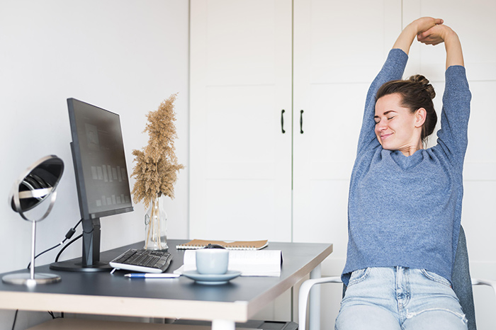 Profissional em home office fazendo alongamento na cadeira durante pausa no trabalho.