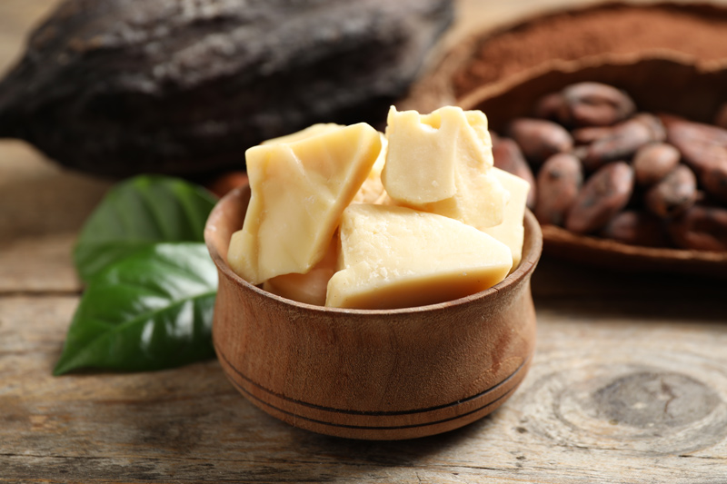 Manteiga de cacau em pedaços ao lado de grãos de cacau e chocolate, ingrediente essencial para chocolate de qualidade. 